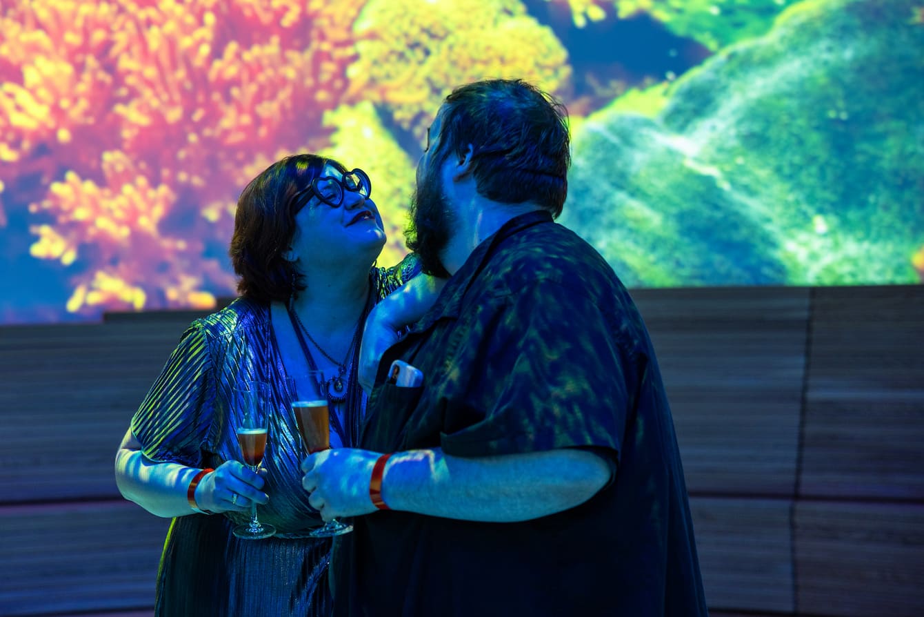 A couple holding champagne flutes leaning in for a kiss.