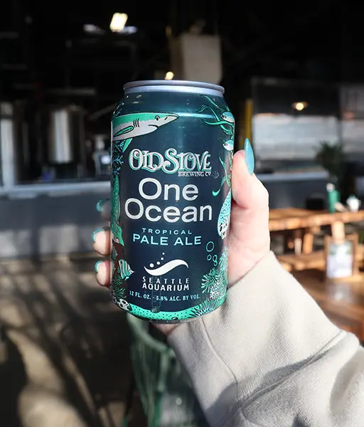 A can of Old Stove Brewery's One Ocean Indian Pale Ale collaboration with the Seattle Aquarium being held by a hand in the sunlight.